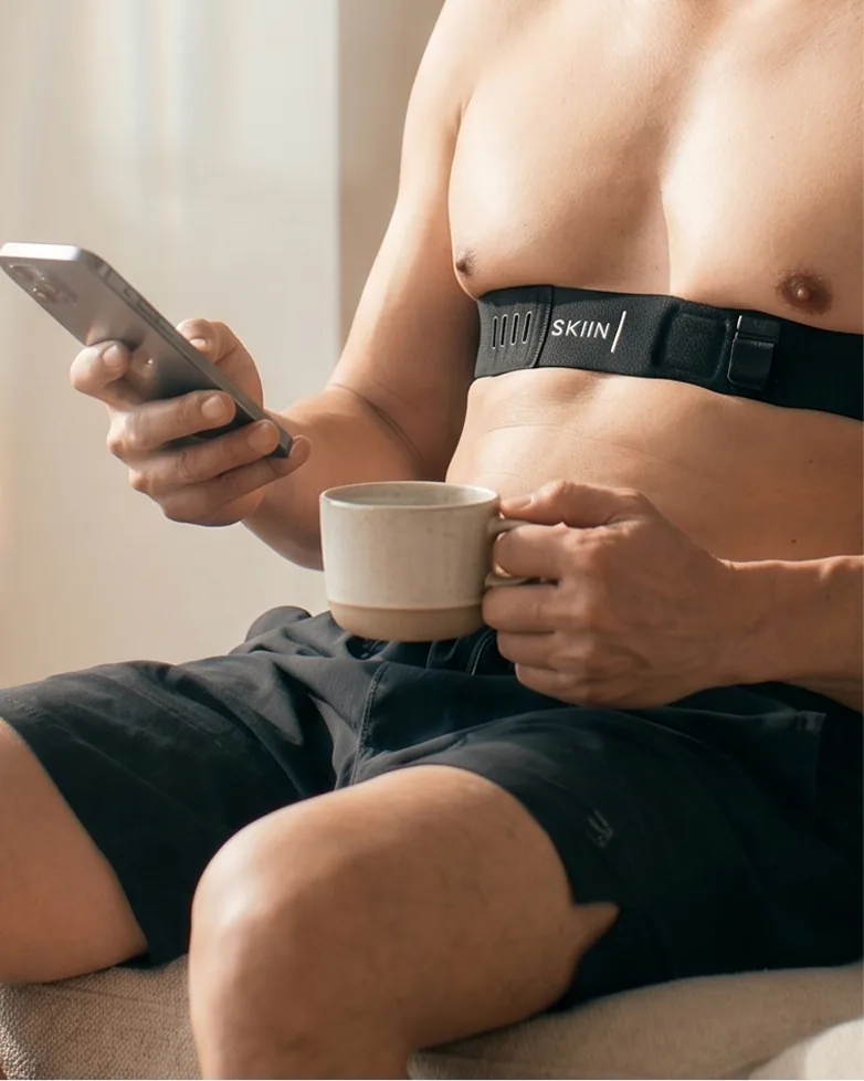 A man at home wearing the SKIIN band, holding his phone and a cup of coffee