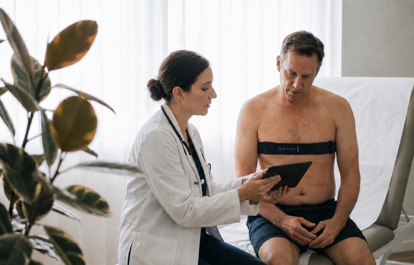 A physician showing a patient their recording on a tablet, the patient wearing the SKIIN chest band