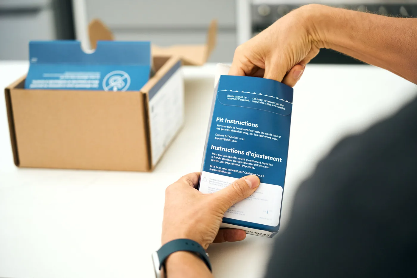 Hands holding the fit instructions beside an opened SKIIN™ shipping box
